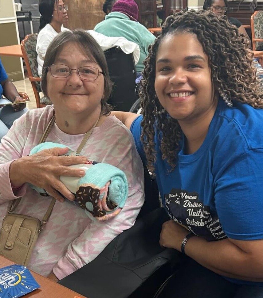 Diversicare team member sitting beside a resident holding a blanket, both smiling together.
