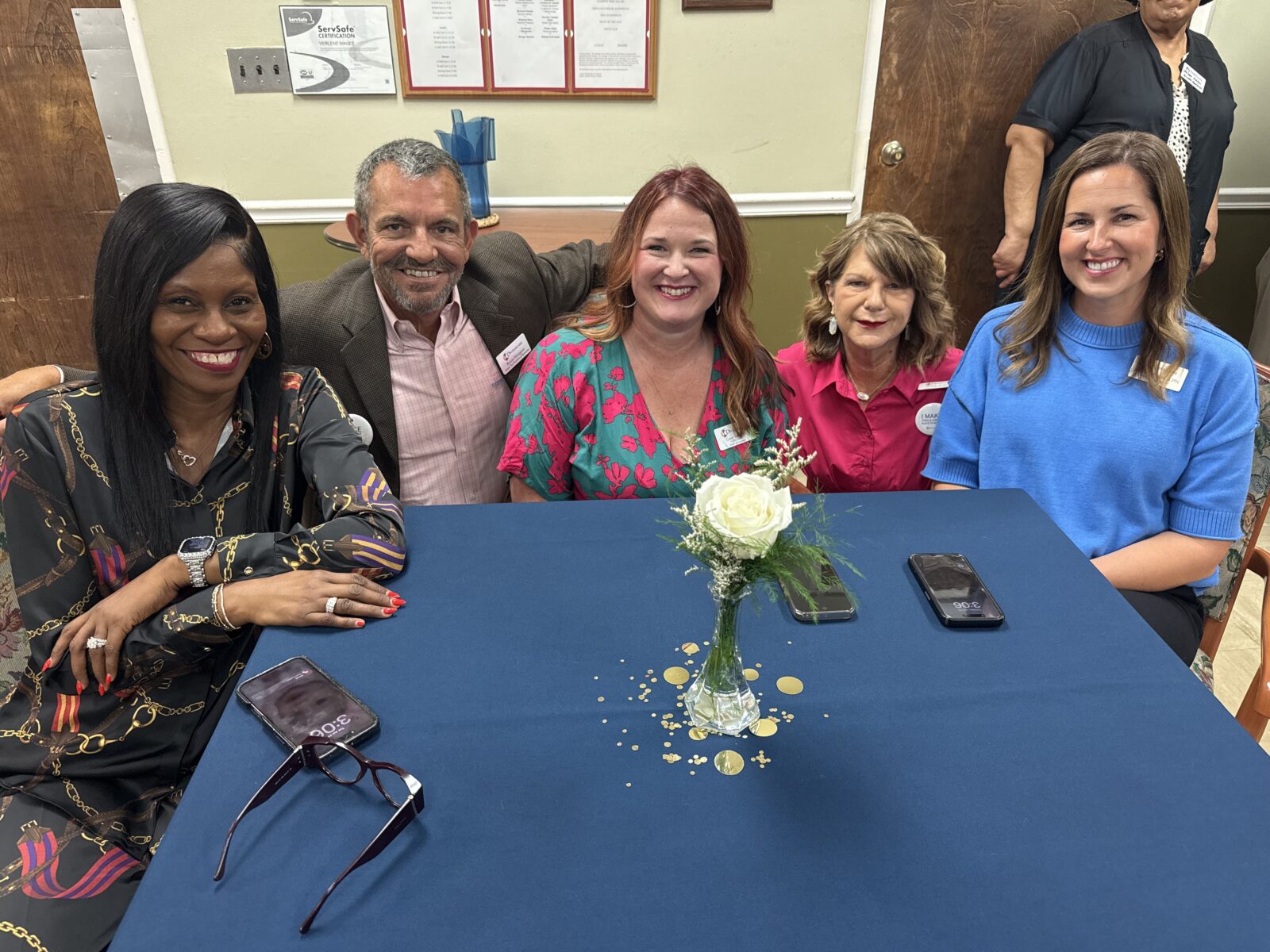 Group of five people sitting at a table smiling. 