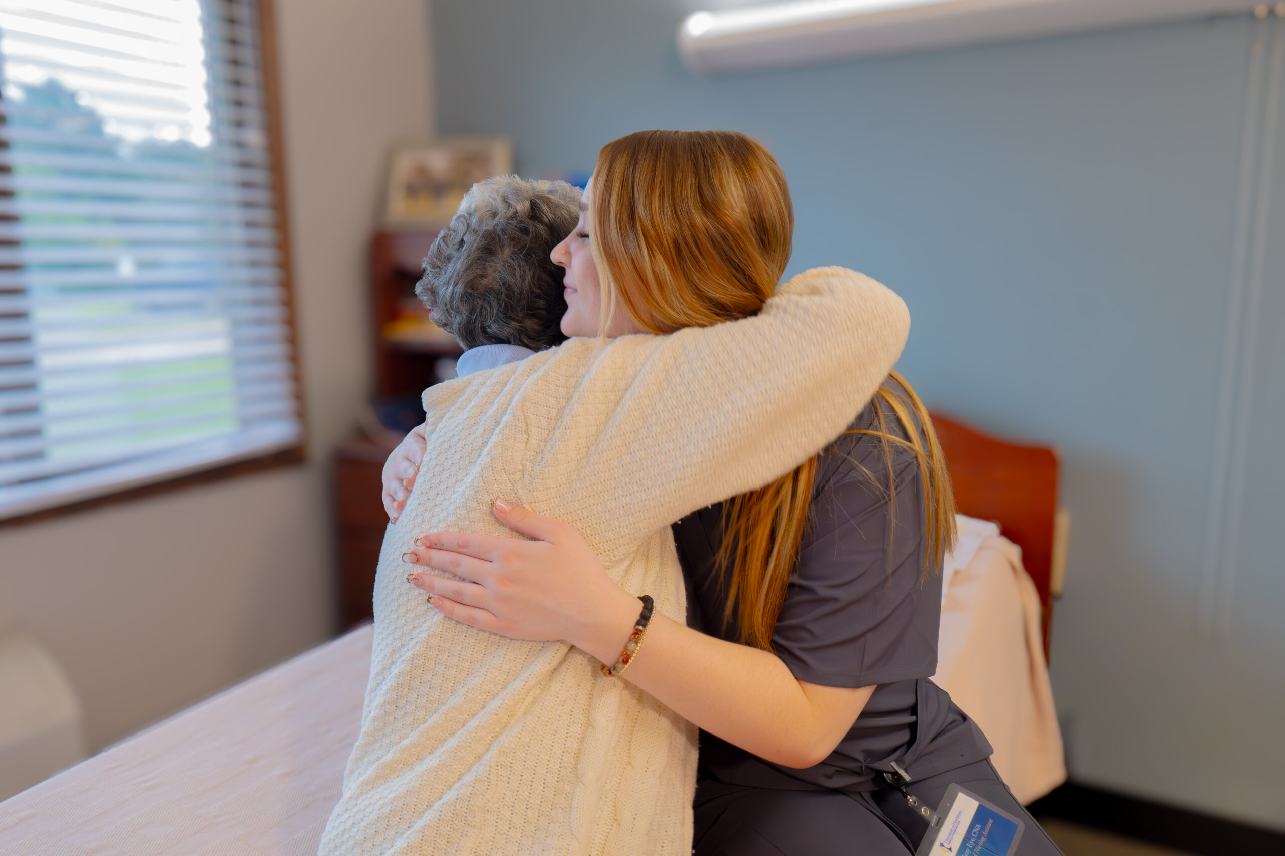 Nurse in medical scrubs warmly hugging a resident at a Diversicare care center.